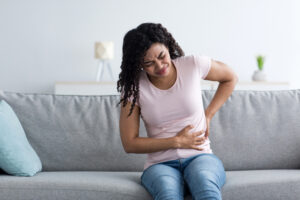 Health care, illness, pain in abdomen, side and back. Sad unhappy young african american sick female suffering from acute kidney pain, injury or muscle spasm in living room interior, empty space